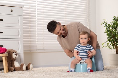 Father training his child to sit on baby potty indoors. Space for text