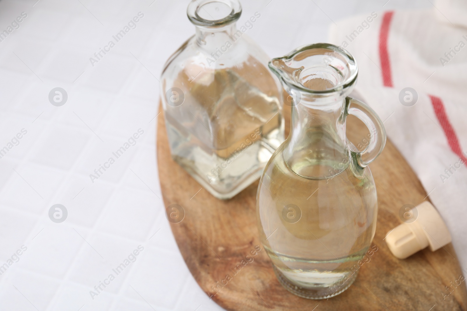 Photo of Vinegar in glass jug and bottle on white tiled table, space for text