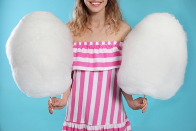 Young woman with tasty cotton candy on blue background, closeup