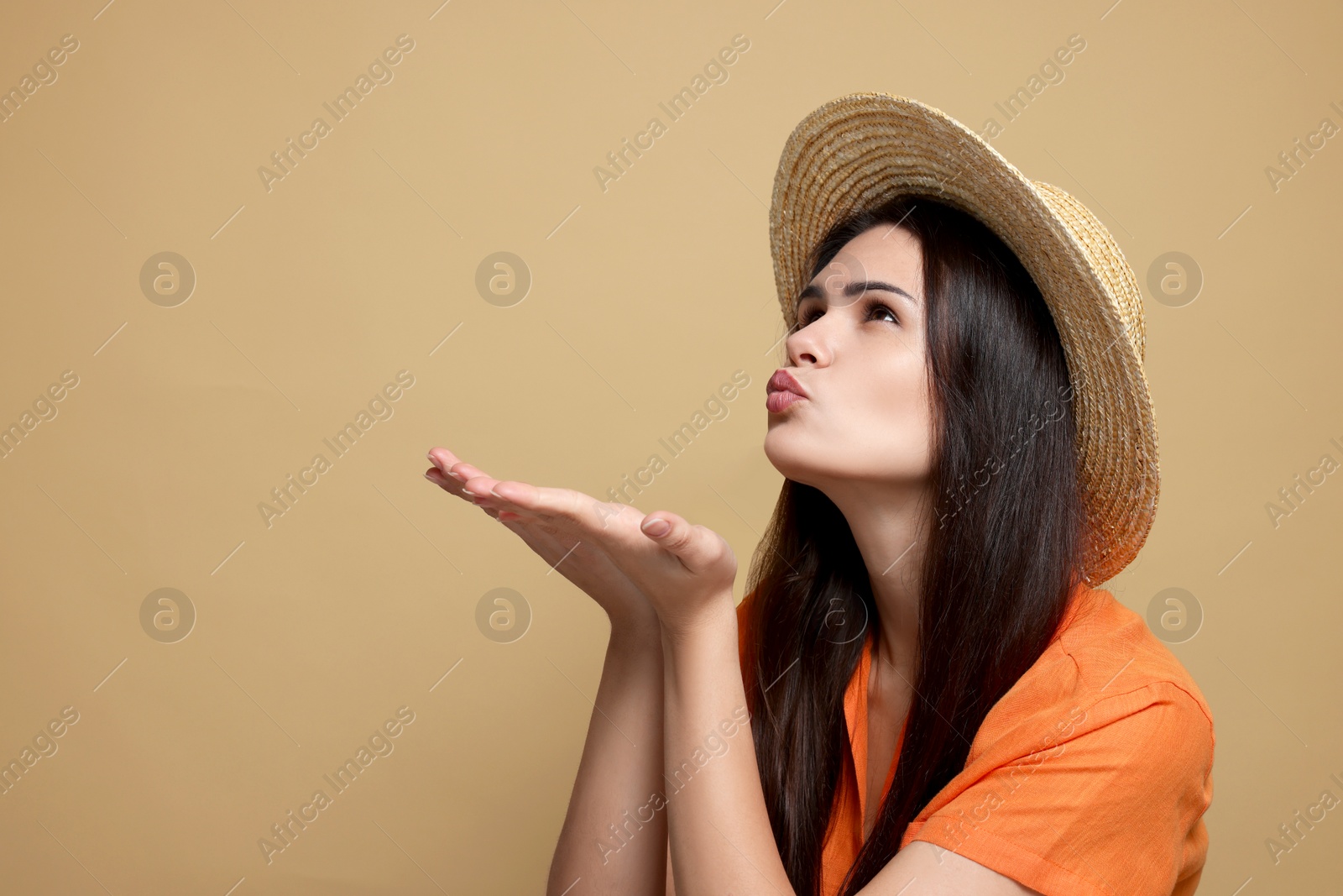 Photo of Beautiful young woman in straw hat blowing kiss on beige background. Space for text