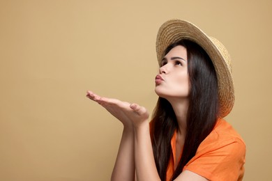 Photo of Beautiful young woman in straw hat blowing kiss on beige background. Space for text