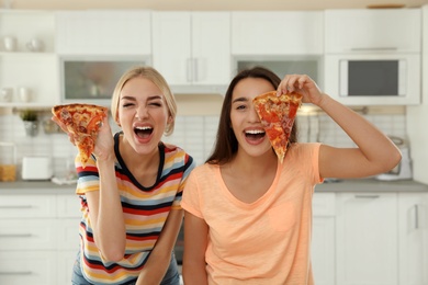 Photo of Young women with tasty pizza laughing in kitchen