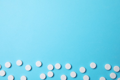 Photo of White pills on light blue background, flat lay. Space for text