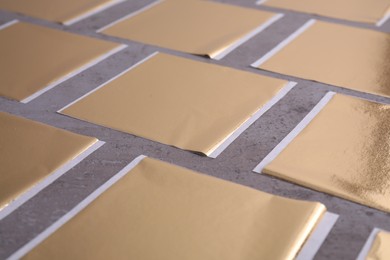 Photo of Many edible gold leaf sheets on grey textured table, closeup