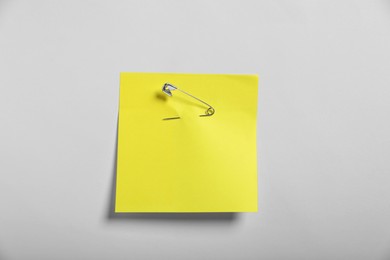 Yellow paper note attached with safety pin to white background, top view