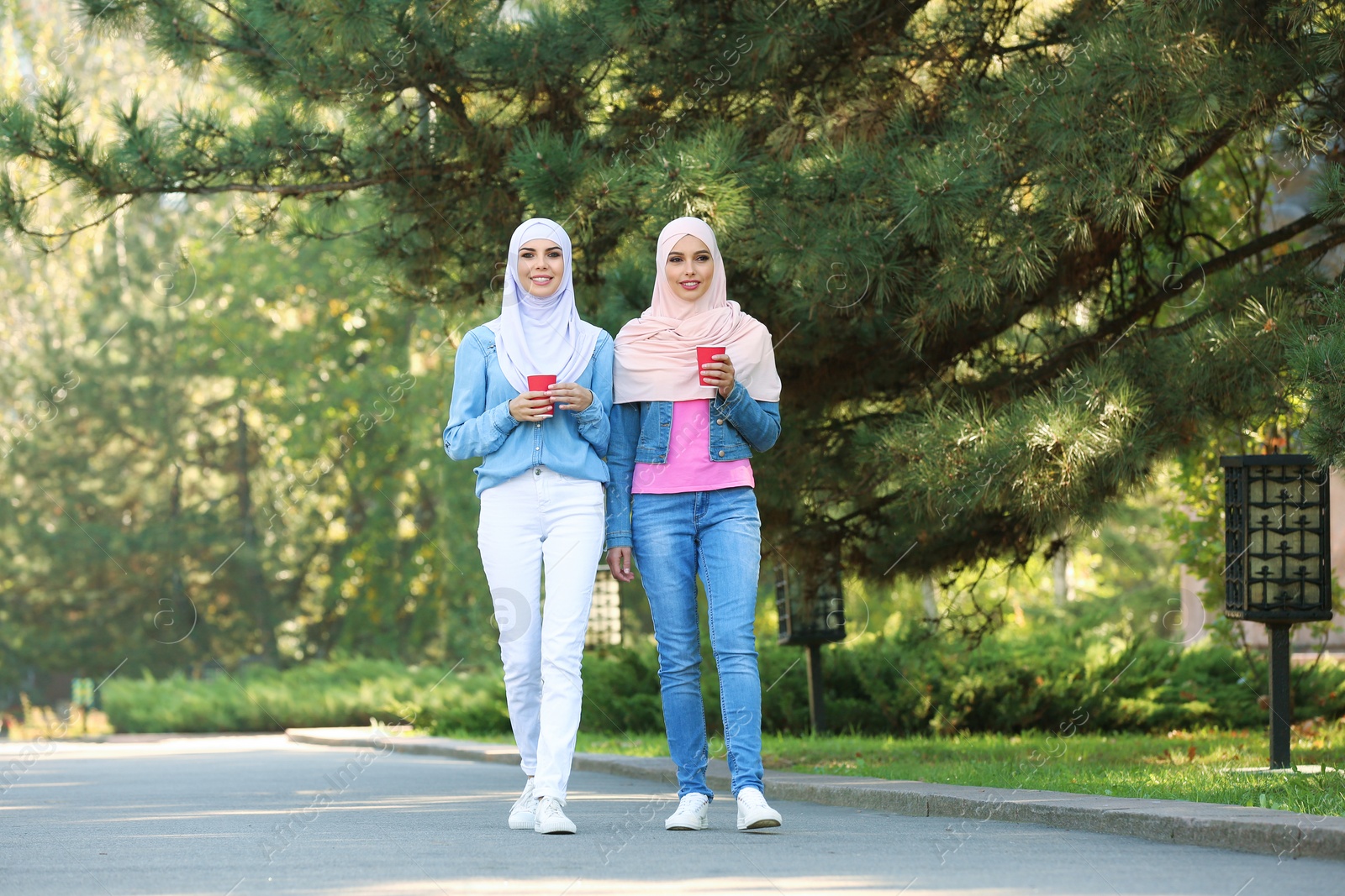 Photo of Muslim women with cups of coffee walking in park