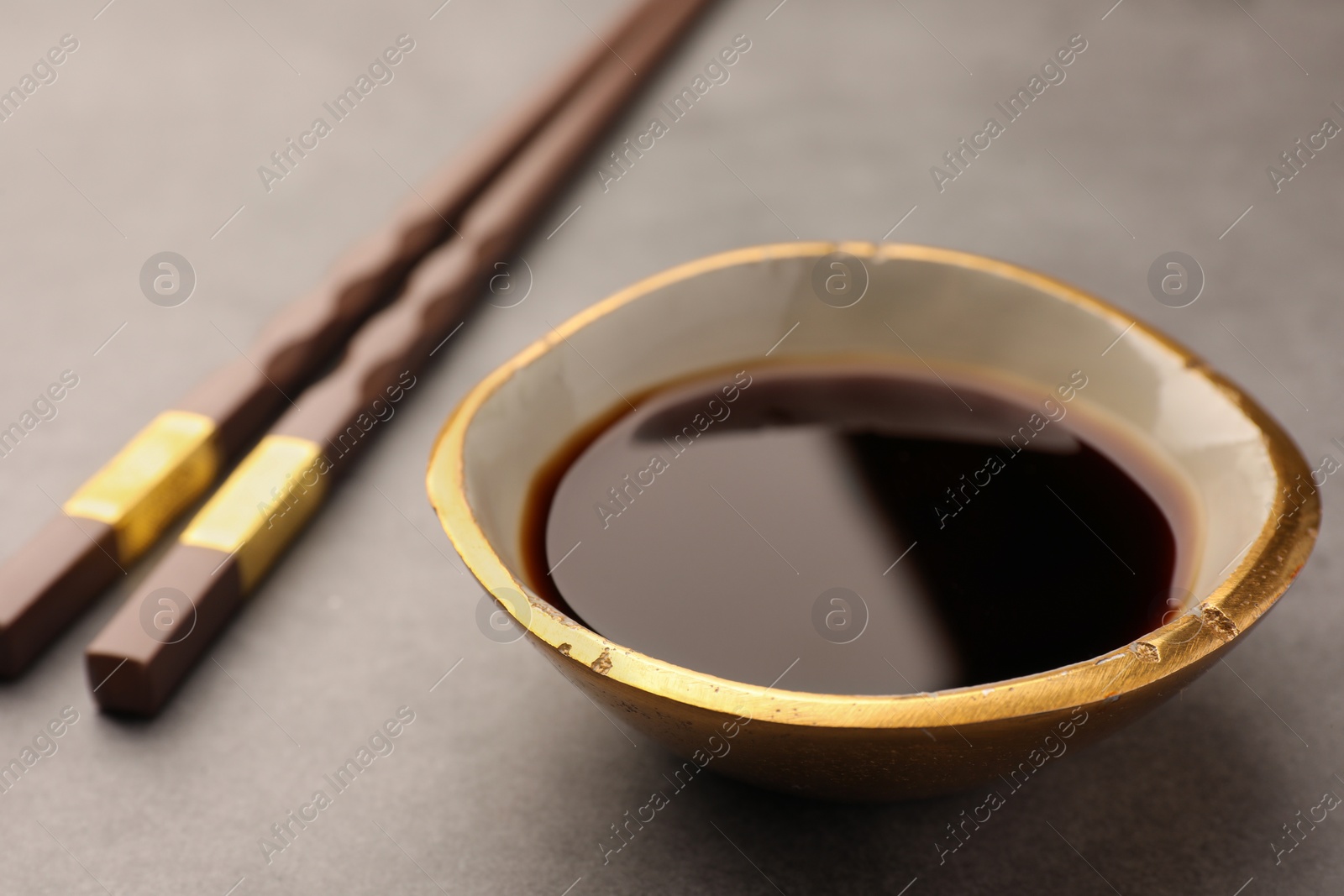 Photo of Bowl of soy sauce and chopsticks on grey table, closeup