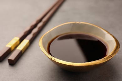 Bowl of soy sauce and chopsticks on grey table, closeup