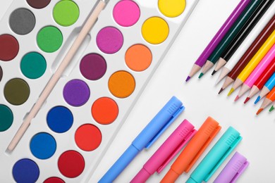 Photo of Watercolor palette, colorful pencils and markers on white background, flat lay