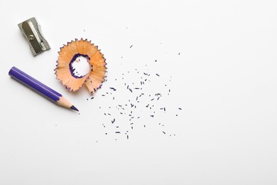 Photo of Purple pencil, shaving, crumbs and sharpener on white background, top view