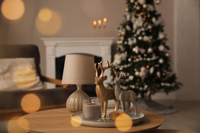 Deer figures, burning candle with lamp on wooden table and Christmas tree in living room