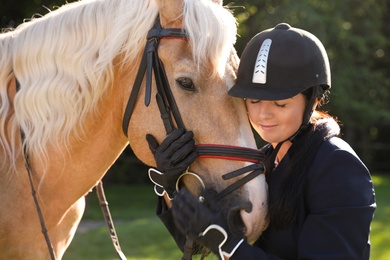 Photo of Young woman in horse riding suit and her beautiful pet outdoors on sunny day