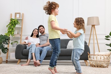 Happy children dancing while their parents looking at them in room