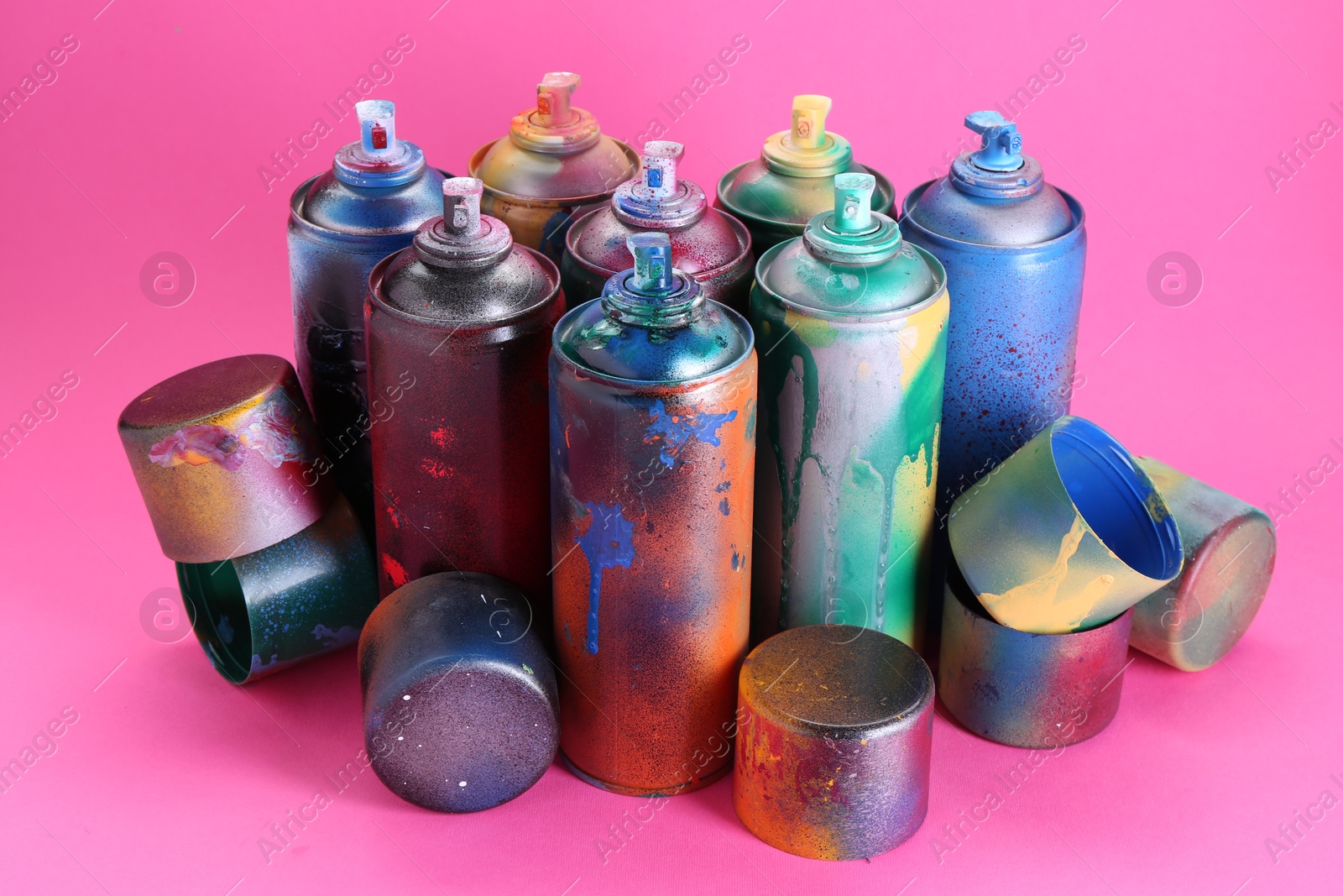 Photo of Many spray paint cans with caps on pink background