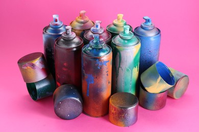 Many spray paint cans with caps on pink background