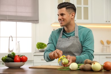 Photo of Man peeling zucchini at table in kitchen. Preparing vegetable