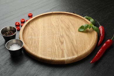 Photo of Cutting board, salt, spices, basil and chili peppers on black textured table. Space for text