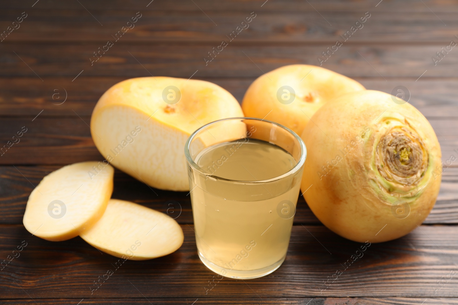 Photo of Glass of fresh natural turnip juice, cut and whole roots on wooden table