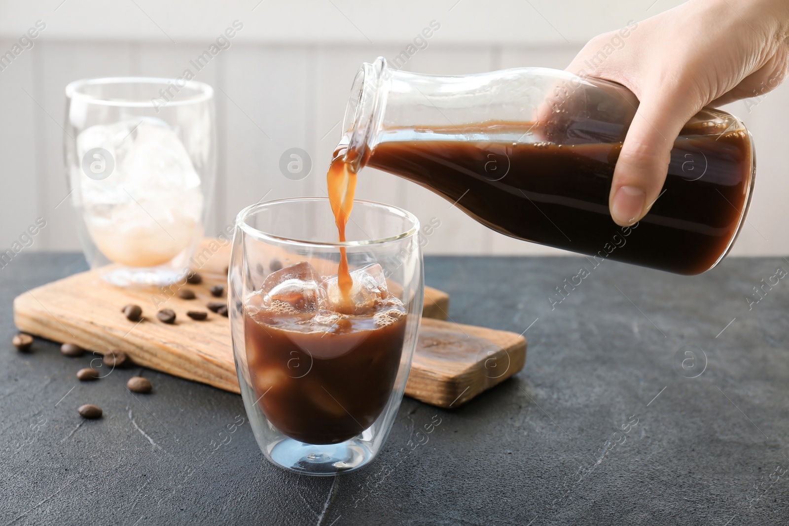 Photo of Woman pouring cold brew coffee into glass on table