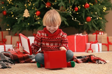 Photo of Little child opening Christmas gift on floor at home