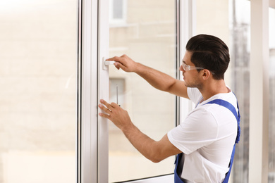 Photo of Construction worker repairing plastic window with screwdriver indoors