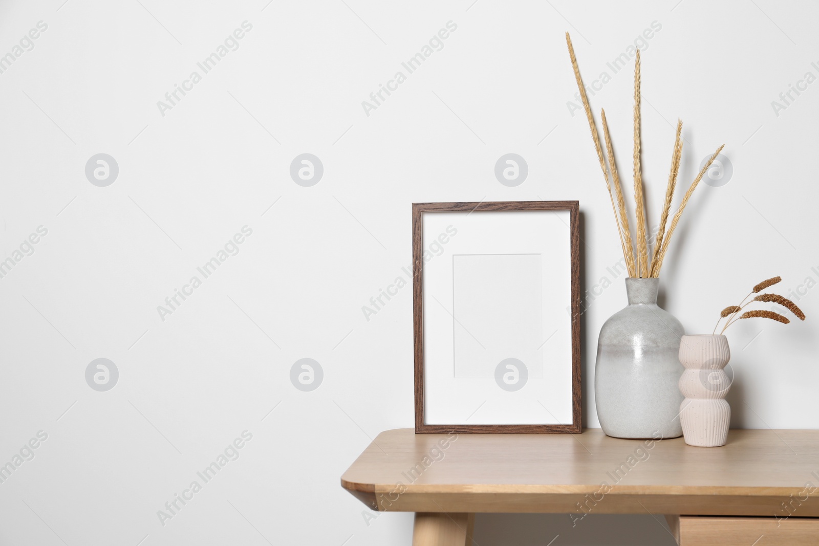 Photo of Empty photo frame and vases with dry decorative spikes on wooden table. Mockup for design