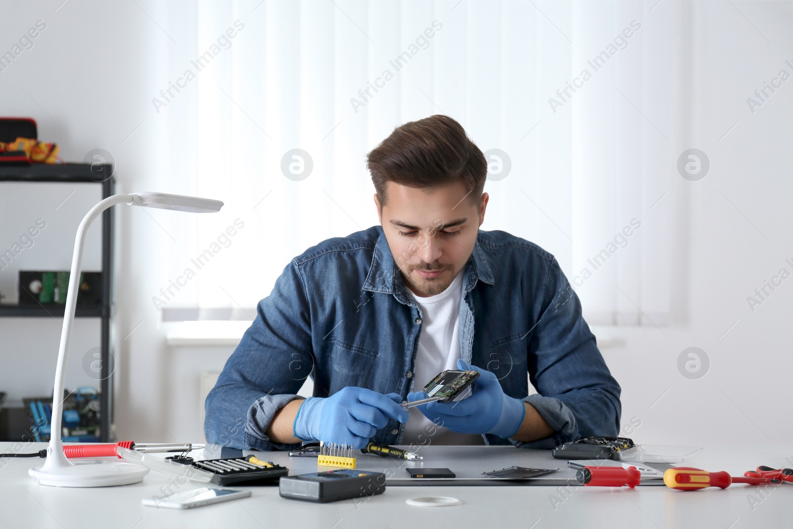 Photo of Technician repairing broken smartphone at table in workshop