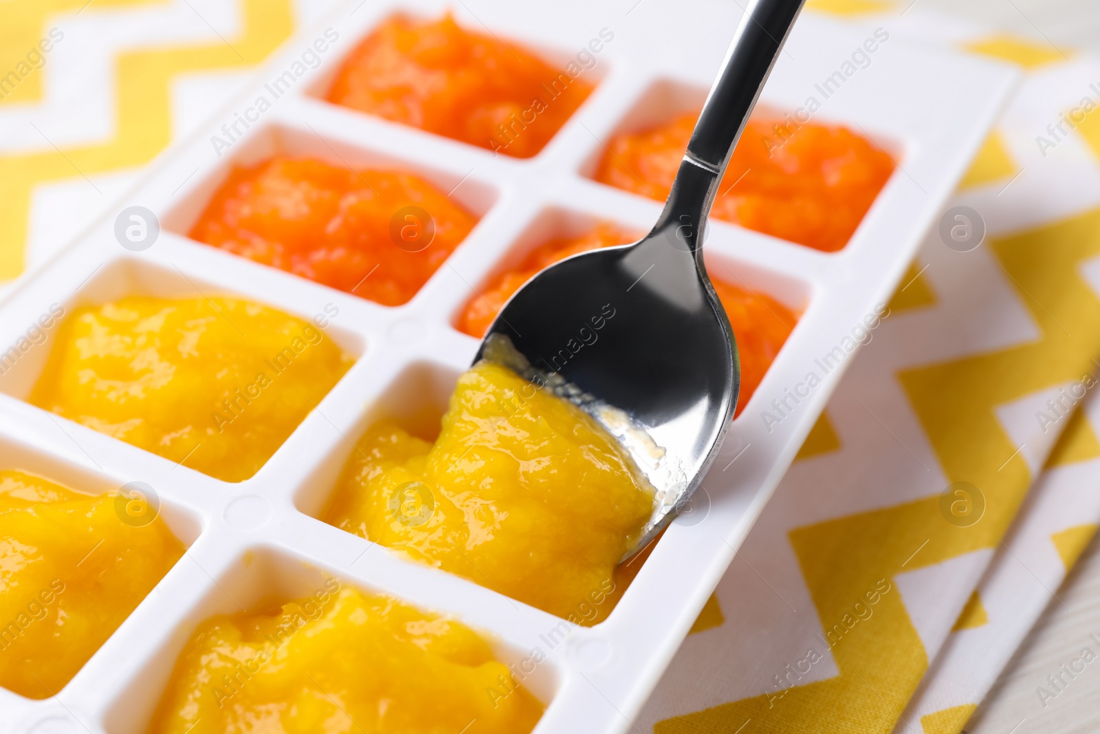 Photo of Putting puree with spoon into ice cube tray on table, closeup. Ready for freezing