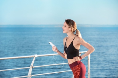 Young woman listening to music and running on pier in morning