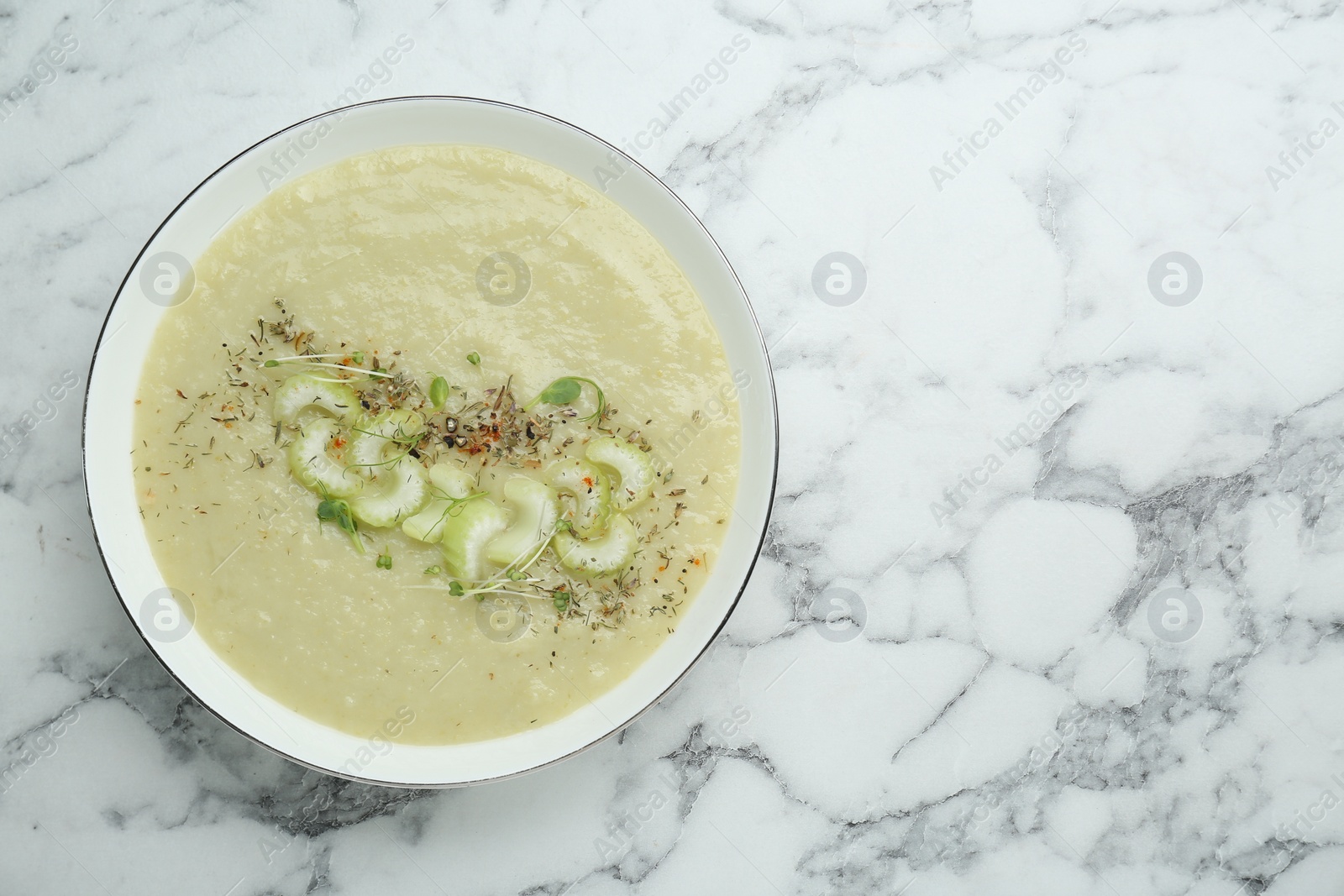 Photo of Bowl of delicious celery soup on white marble table, top view. Space for text