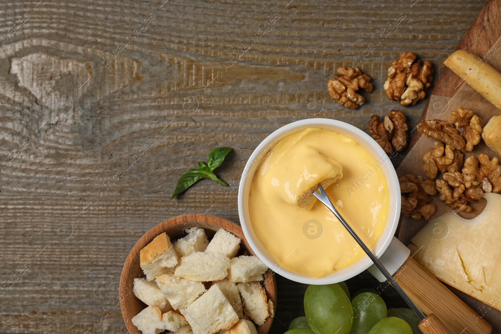 Photo of Flat lay composition with pot of tasty cheese fondue and products on wooden table, space for text