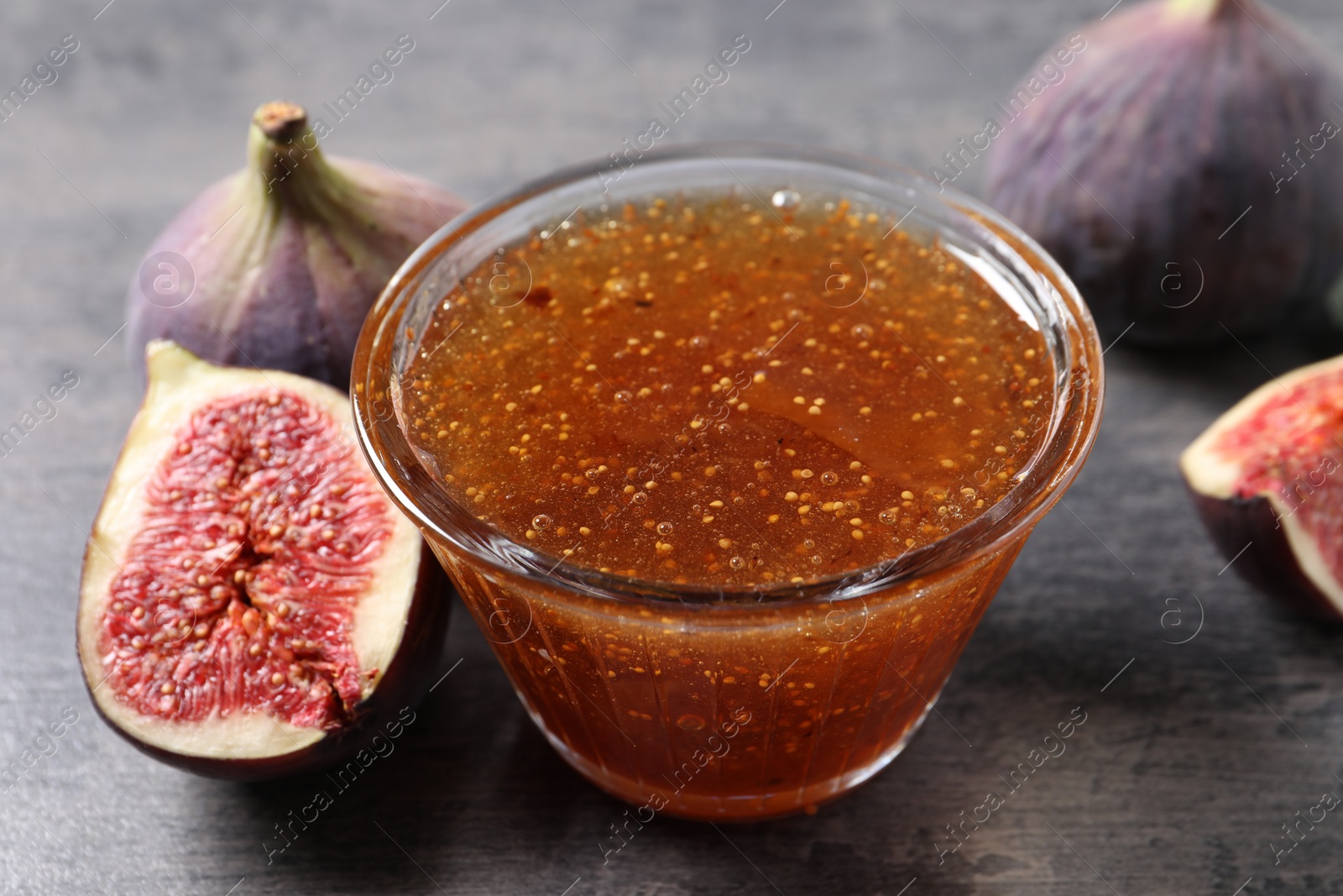 Photo of Bowl with tasty sweet jam and fresh figs on grey table, closeup