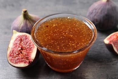 Bowl with tasty sweet jam and fresh figs on grey table, closeup