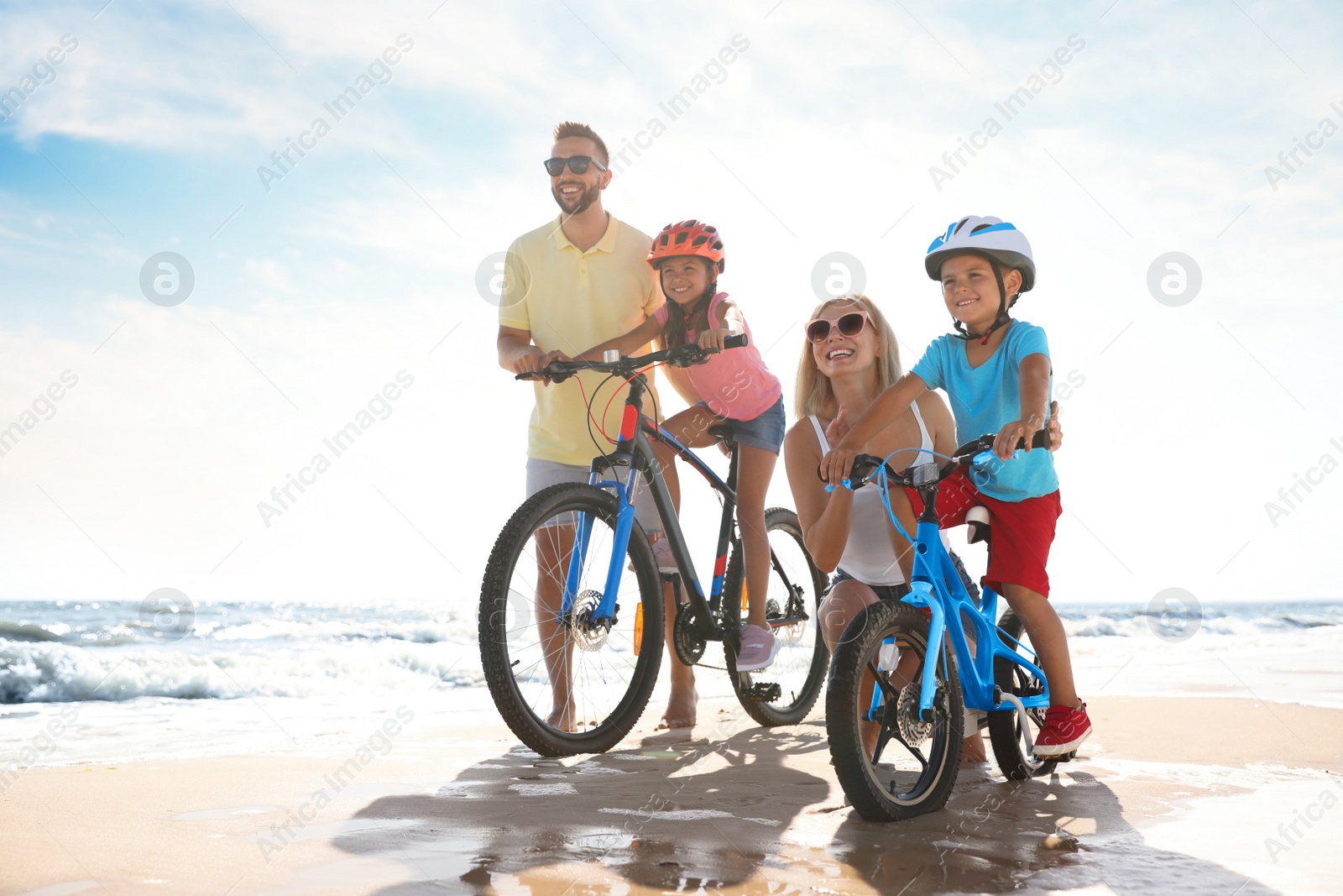 Photo of Happy parents teaching children to ride bicycles on sandy beach near sea