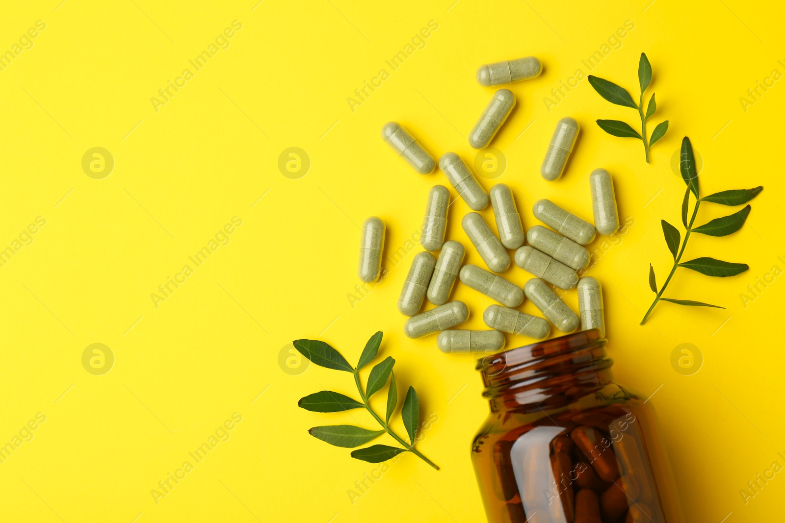 Photo of Vitamin pills, branches and bottle on yellow background, flat lay. Space for text