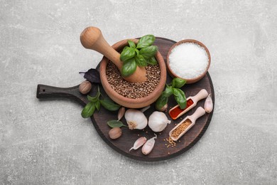 Mortar with pestle and different spices on light grey table, above view