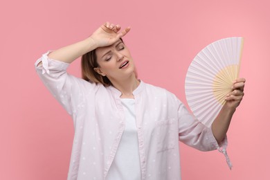 Photo of Beautiful woman waving hand fan to cool herself on pink background
