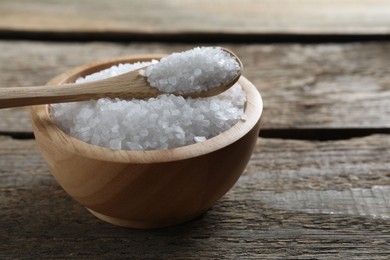 Photo of Organic salt in bowl and spoon on wooden table, closeup. Space for text