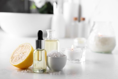 Essential oils, sea salt and lemon on white table in bathroom, closeup. Space for text