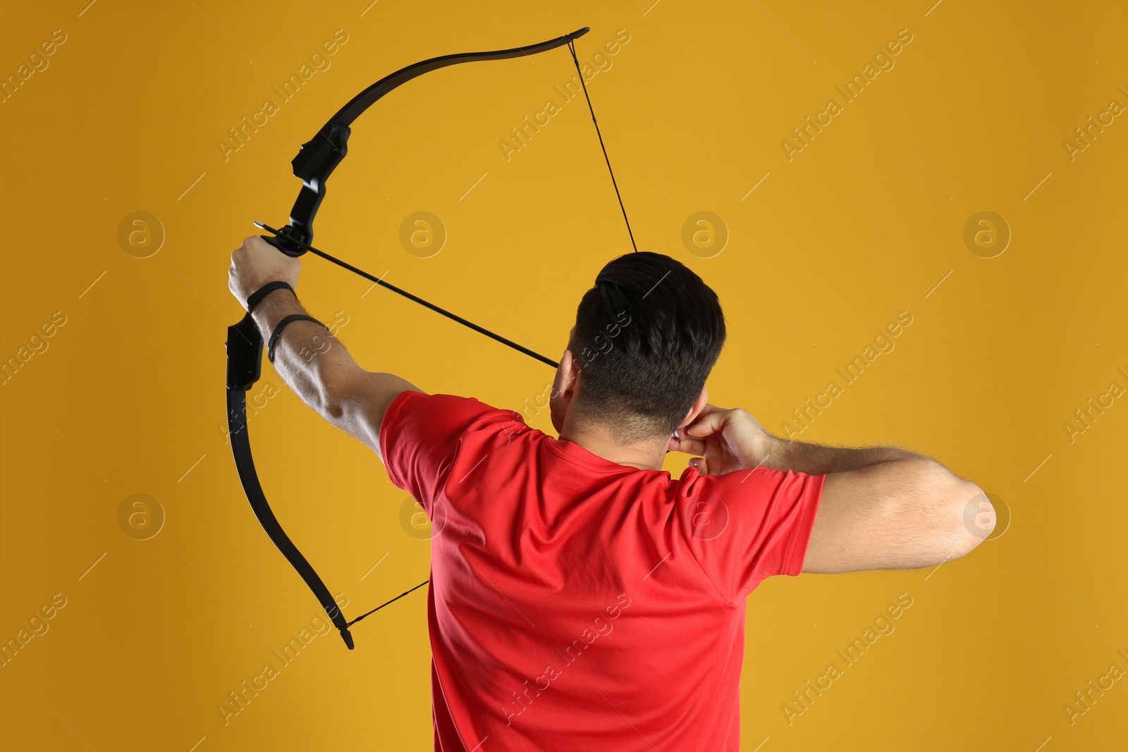 Photo of Man with bow and arrow practicing archery on yellow background, back view