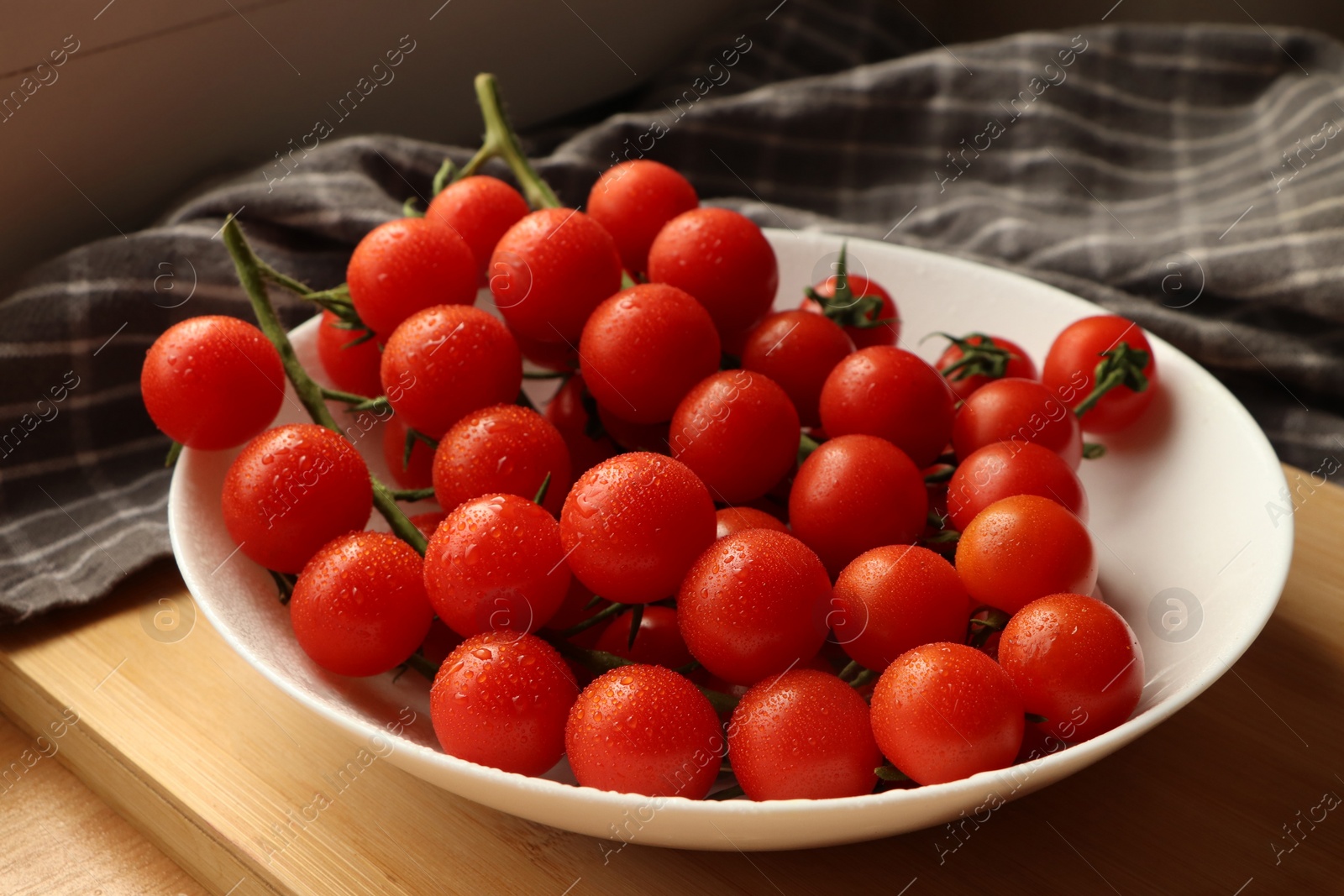 Photo of Plate of ripe whole cherry tomatoes with water drops on wooden table, closeup