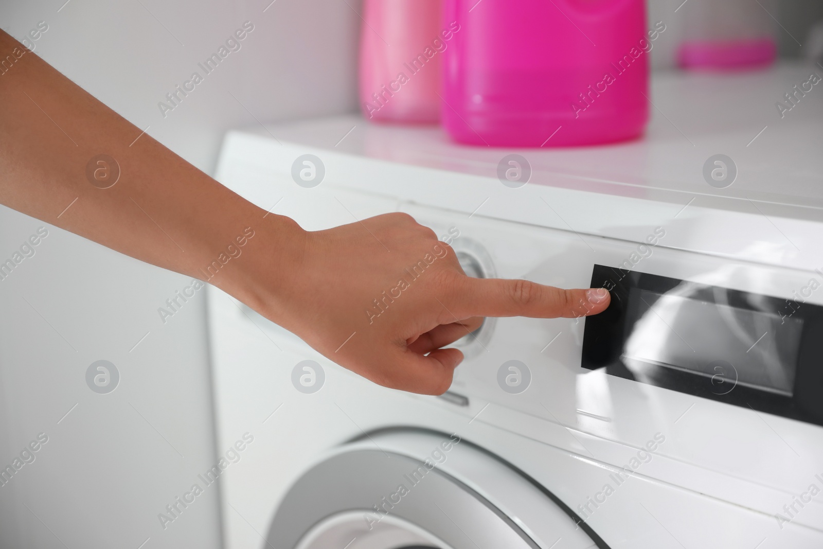 Photo of Woman pressing button on washing machine in bathroom, closeup