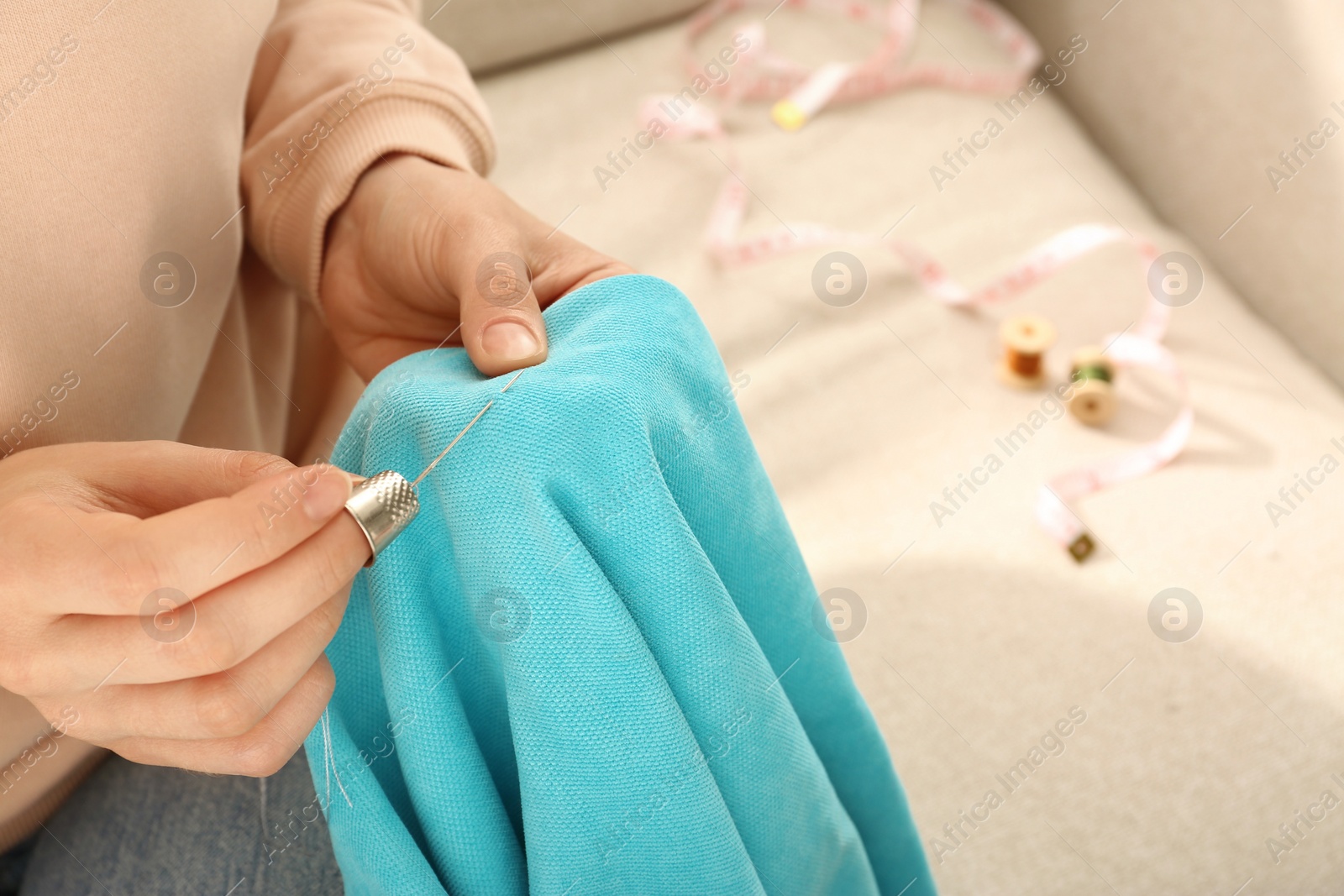 Photo of Woman sewing on turquoise fabric with thimble and needle indoors, closeup. Space for text