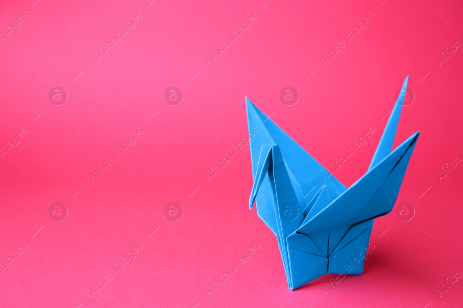 Photo of Origami art. Handmade paper crane on pink background, space for text