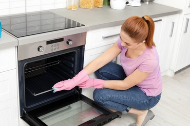 Photo of Woman cleaning oven rack with rag in kitchen