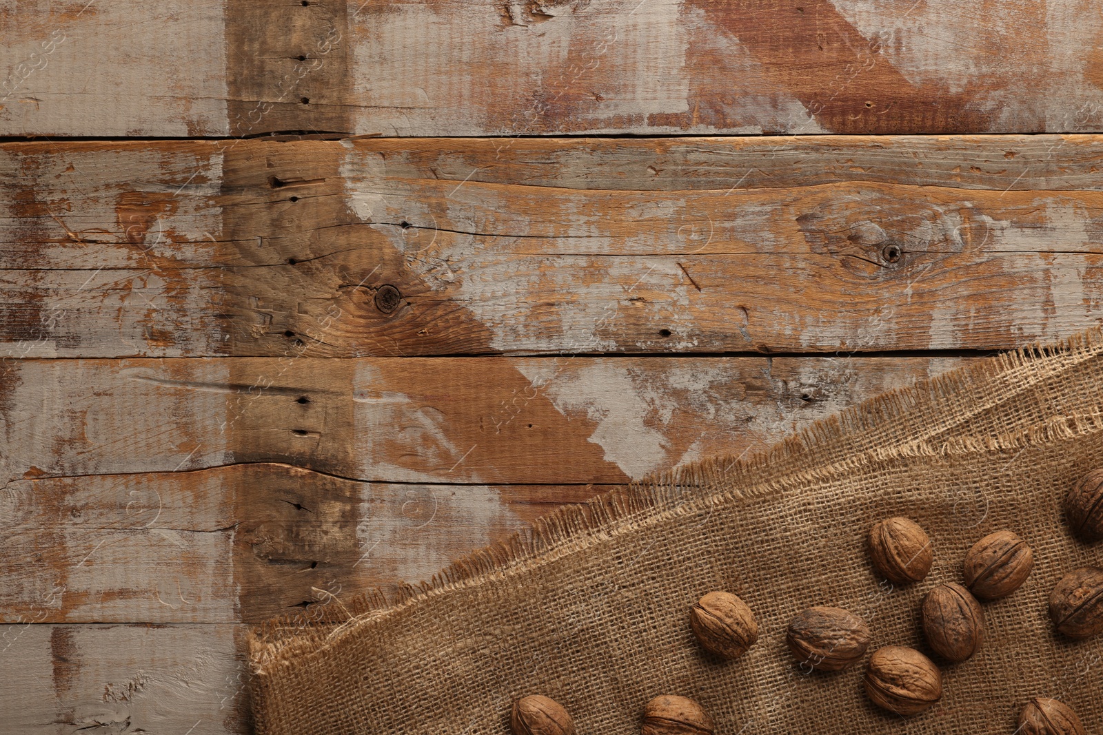 Photo of Burlap fabric and walnuts on wooden table, top view. Space for text