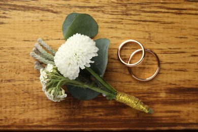 Photo of Small stylish boutonniere and rings on wooden table, flat lay