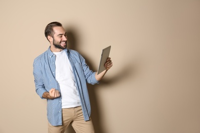 Photo of Emotional young man with tablet celebrating victory on color background. Space for text