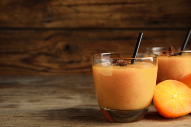 Tasty persimmon smoothie with anise and straw on wooden table. Space for text