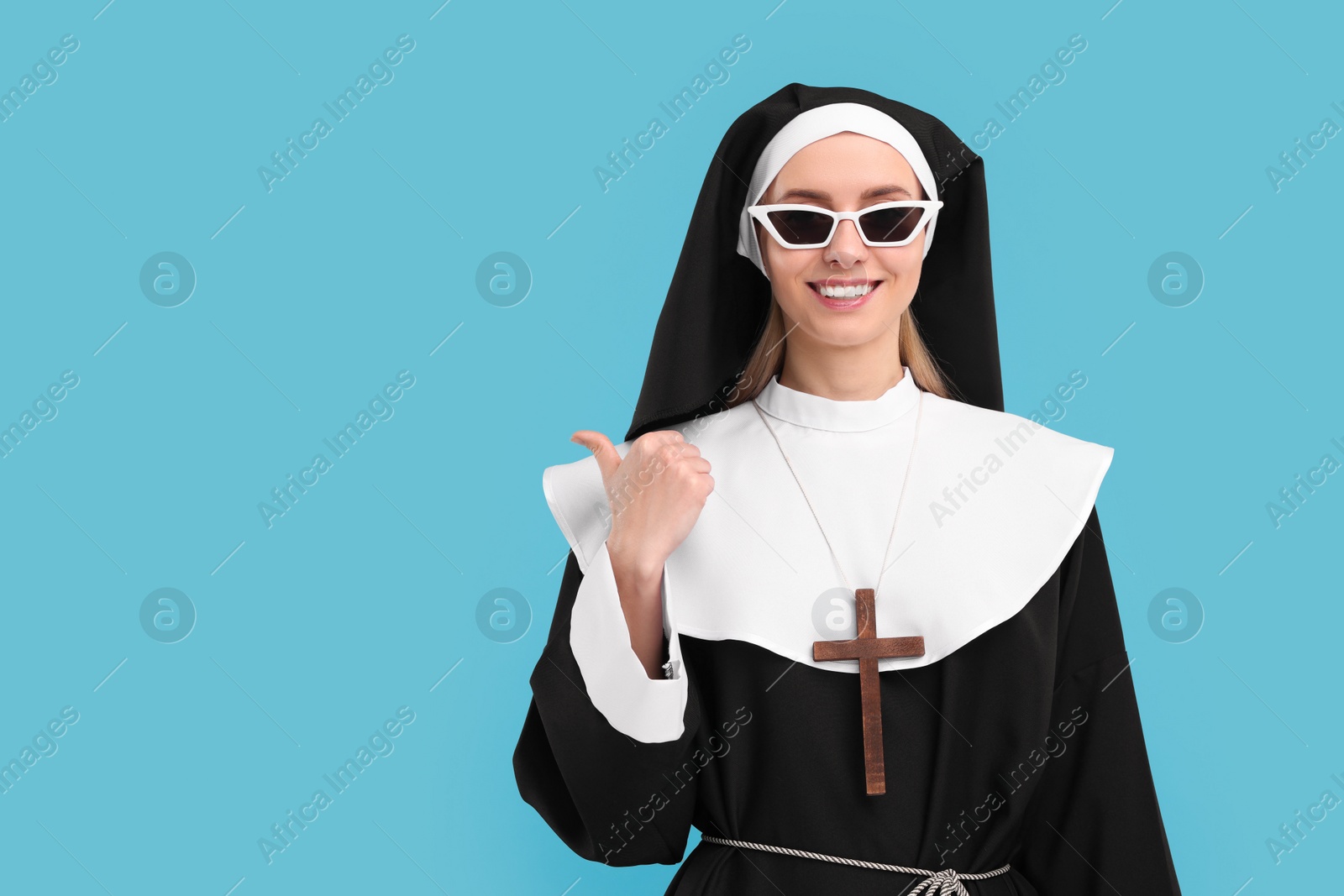 Photo of Happy woman in nun habit pointing at something against light blue background. Space for text